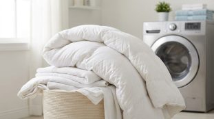 Panier à linge rempli de draps et d'une couette blanche devant une machine à laver moderne.